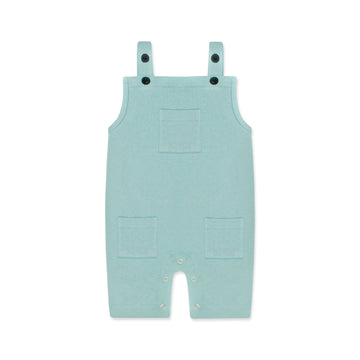 A pastel blue newborn romper with button-on-shoulder straps and front pockets, displayed against a light background with orange and green design elements. The text highlights features like 'Button on Shoulder,' 'Pockets,' and 'New Arrivals.' The brand name 'Palm and Pale' and website 'palmandpale.com' are also visible. The tagline reads 'Sunny styles for little smiles.'