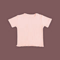 A baby short-sleeved T-shirt in a soft pastel pink color, displayed against a muted brown background. The T-shirt is made from ribbed fabric and features snap buttons on one shoulder for easy dressing. The hem has a subtle wavy finish, adding a delicate touch to the design.