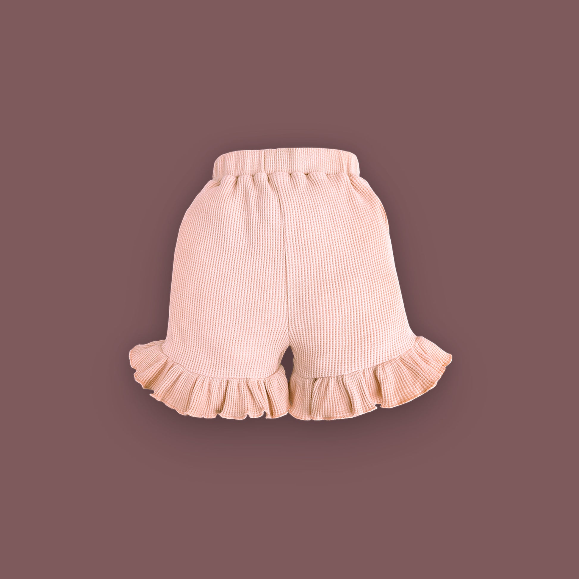 A pair of baby shorts in a soft pastel pink color, displayed against a muted brown background. The shorts are made from ribbed fabric and feature an elastic waistband for comfort. The leg openings are adorned with delicate ruffled hems, adding a cute and stylish touch.