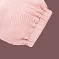 A close-up view of a baby garment in soft pastel pink, showcasing the elastic waistband detail. The fabric has a ribbed texture, and the gathered elastic design ensures a comfortable and snug fit. The muted brown background highlights the fine stitching and gentle stretch of the material.
