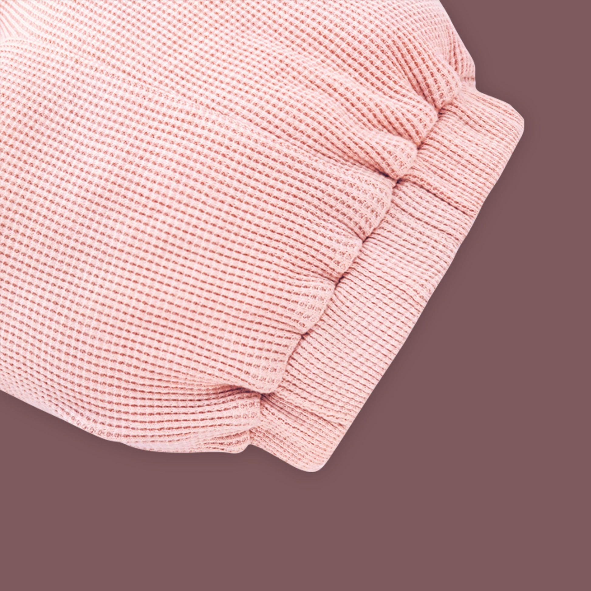 A close-up view of a baby garment in soft pastel pink, showcasing the elastic waistband detail. The fabric has a ribbed texture, and the gathered elastic design ensures a comfortable and snug fit. The muted brown background highlights the fine stitching and gentle stretch of the material.