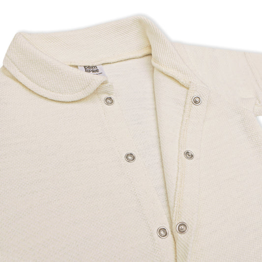 A soft, cream-colored newborn baby romper with a rounded collar, short sleeves, and short legs. The romper features snap buttons down the front for easy dressing. The background includes playful doodles, text highlighting key features like 'Snap Button' and 'Short Sleeves & Legs,' along with 'New Arrivals' branding from Palm and Pale. The tagline at the bottom reads 'Sunny styles for little smiles.'