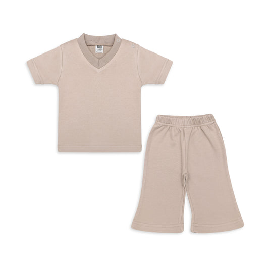 Newborn baby outfit featuring a soft beige V-neck T-shirt with snap buttons on the shoulder and matching pajama pants. The set is designed for comfort and ease, perfect for delicate baby skin. The background includes playful elements with text highlights like 'New Arrivals' and 'Sunny styles for little smiles.' Brand logo and website 'palmandpale.com' are also included.